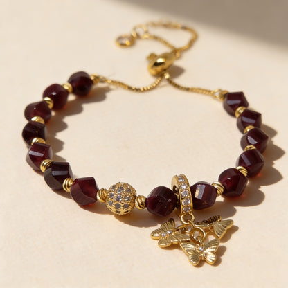 Handmade garnet gemstone bracelet with gold-plated accents, zircon pavé bead and butterfly charms on a neutral background.